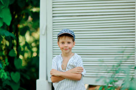 on the street against white shutters is a cute little boy in a capの写真素材
