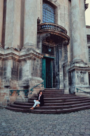 on the steps of the old temple sits a woman in a black coat