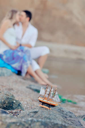 against the background of a young couple sitting on a sand model of a sailing shipの写真素材