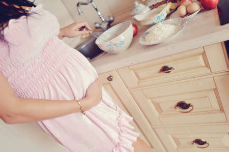 in the kitchen pregnant woman in a pink dress preparing breakfastの写真素材