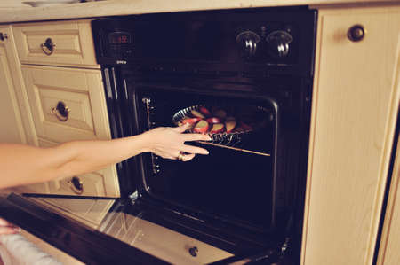 female hand puts in the oven with a baking apple pieの写真素材