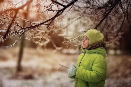 boy in a green suit walks in the park in winter with frozen trees and grassの写真素材