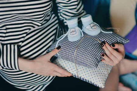 pregnant woman in a striped vest keeps the cushions baby shoesの写真素材