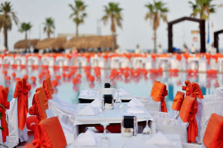 Outdoors under palm trees by the pool decorated with orange bows banquet tablesの写真素材