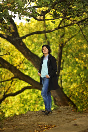 on the background of trees in autumn woman in a black coat and trousers for a walk in the parkの写真素材