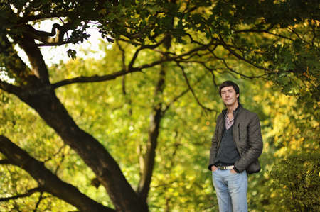 against the backdrop of autumn trees man in jacket and jeans for a walk in the parkの写真素材