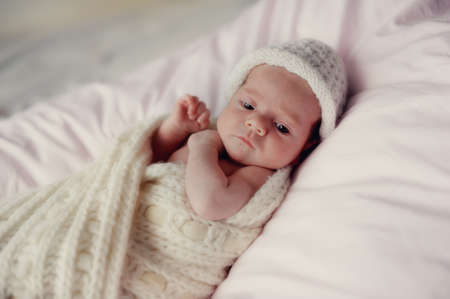 little baby wrapped in a knitted blanket and a white knitted capの写真素材