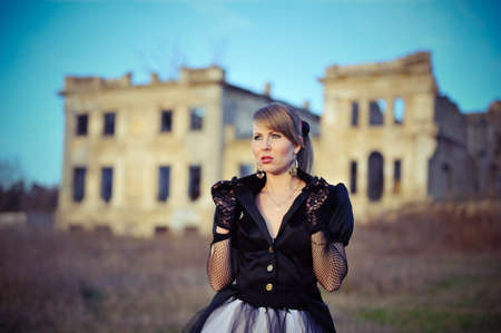 against the background of an old abandoned building blonde girl in a black dress and glovesの写真素材