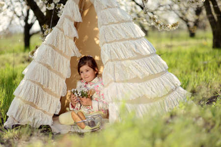 in the lush spring garden on the grass in a tent sits a little girl on vacationの写真素材
