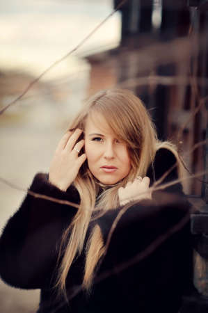 Outdoors portrait of a girl with long blond hair in a black fur coatの写真素材