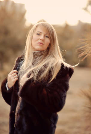 Outdoors portrait of a girl with long blond hair in a black fur coatの写真素材