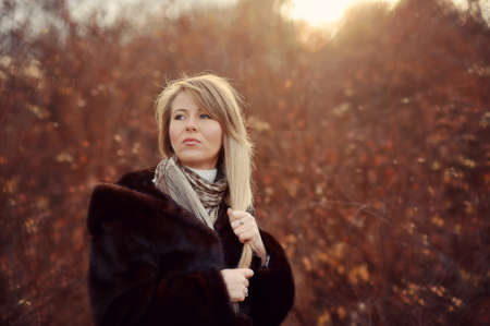 Outdoors portrait of a girl with long blond hair in a black fur coatの写真素材
