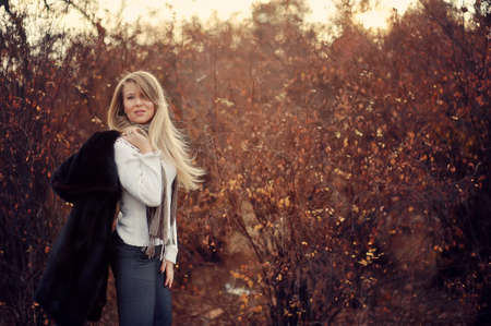 Outdoors portrait of a girl with long blond hair in a black fur coatの写真素材