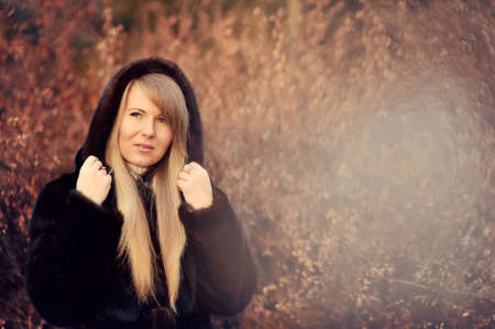Outdoors portrait of a girl with long blond hair in a black fur coatの写真素材