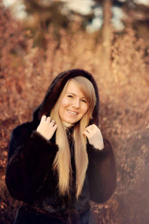 Outdoors portrait of a girl with long blond hair in a black fur coatの写真素材