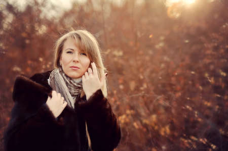 Outdoors portrait of a girl with long blond hair in a black fur coatの写真素材