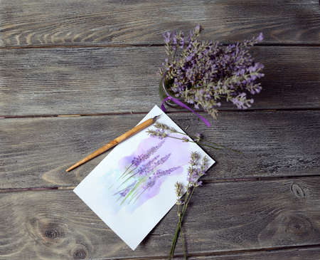 on a wooden table is a vase with a bouquet of lavender and painting byの写真素材