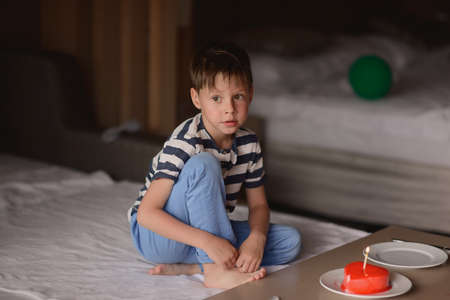 in a room on a bed and boy sitting on a table with a candle cakeの写真素材