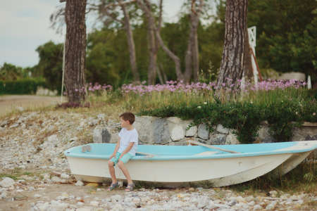 in a forest on the banks of a little boy sitting on the boat and looks into the distanceの写真素材