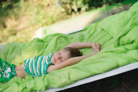 Outdoors in the green stands the white bed with a little cute boyの写真素材
