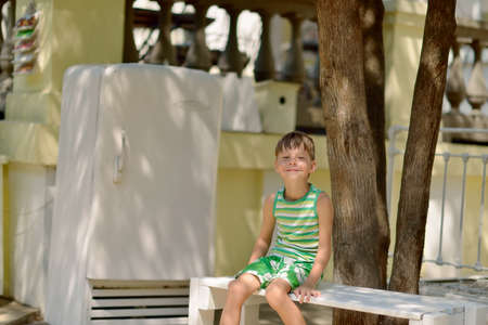 in the courtyard of the house under a tree on the bench sits a boyの写真素材