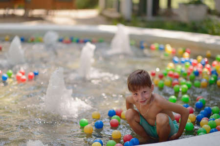 fountain in a lot of multicolored balls and little boy bathes in itの写真素材