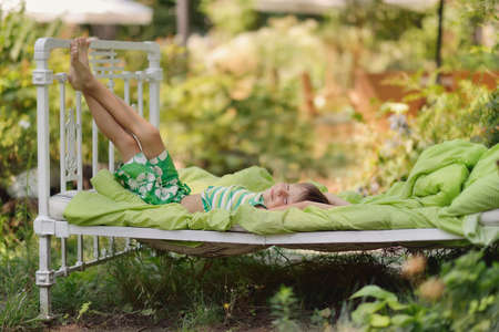 Outdoors in the green stands the white bed with a little cute boyの写真素材