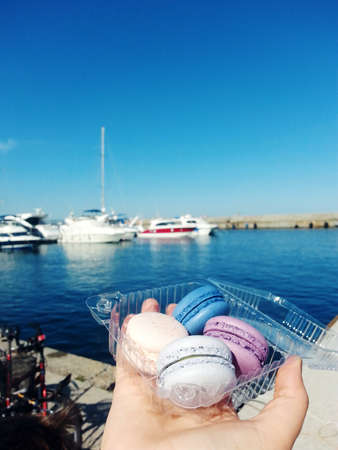 colorful traditional French Macarons in the ranks in the box on the background of the sea and yachtsの写真素材