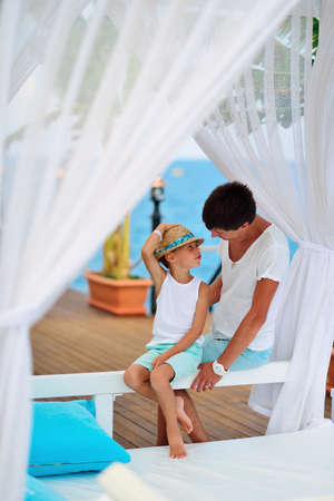 on the background of the sea under a canopy dad with a young son in a hat carrying on a conversationの写真素材