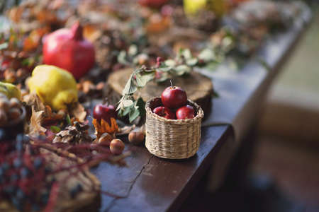 leaves on a wooden table with lemon, pomegranate and a basket with red applesの写真素材