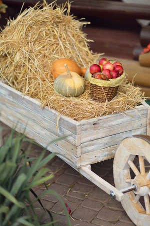 wooden cart with stack of hay, pumpkins and a basket with red applesの写真素材