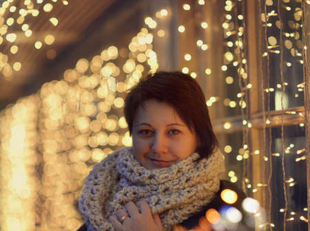 against the evening box with lights garlands woman in knitted scarfの写真素材