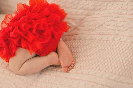 baby lying in bed with her bare legs in red fishnet shortsの写真素材