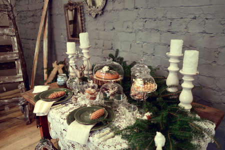 table with Christmas decorations and white large candles, glassware, green cones tree branchの写真素材