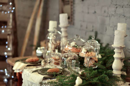 table with Christmas decorations and white large candles, glassware, green cones tree branch