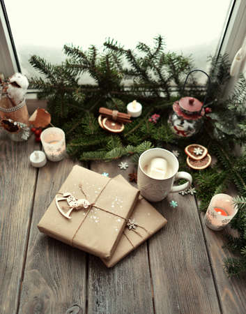window on a wooden window sill branches green tree gifts and cup with cocoa and candlesの写真素材