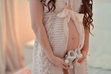 pregnant woman in a knitted jacket with a bow in his hands holding baby bootsの写真素材
