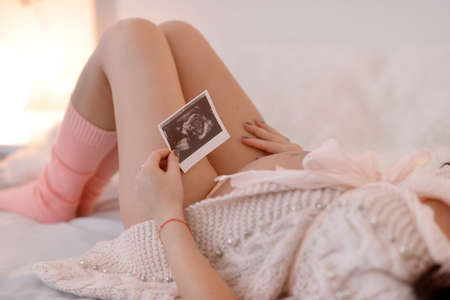 lying on the big bed Pregnant woman in pink socks ultrasound photoの写真素材