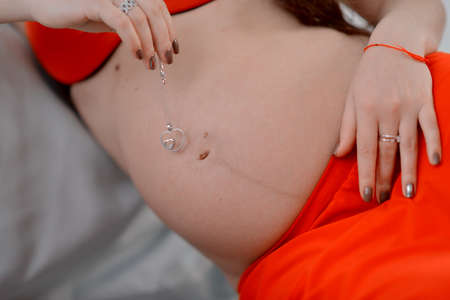 belly of a pregnant woman in a red dress and holding a heart in his handsの写真素材