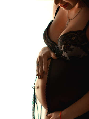 standing at the window pregnant woman in black underwear and hands holding bellyの写真素材