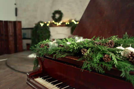against the background of the fireplace and Christmas decorations piano decorated with green branches with cones and candlesの写真素材