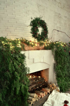 large fireplace in the house with lights and decorated with green needles Christmas wreath with pine conesの写真素材