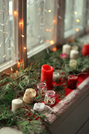 box decorated with a garland of pine needles on the windowsill and a lot of different candlesの写真素材