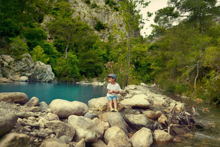against the backdrop of mountains and trees by the lake on the rocks sits a little boyの写真素材