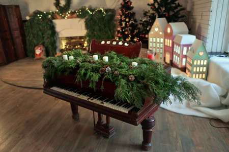 a room with a fireplace and Christmas decorations a piano decorated with green branches with cones and candlesの写真素材