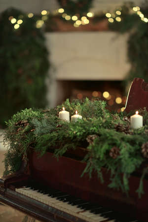 against the background of the fireplace and Christmas decorations piano decorated with green branches with cones and candlesの写真素材