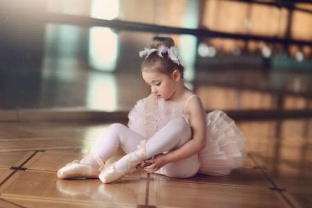 in the hall on the background of large mirrors on the floor sits a little ballerina in white tutuの写真素材