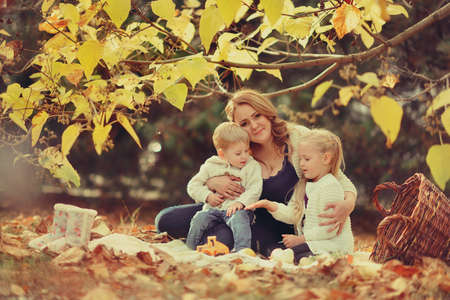 sunny autumn forest resting sitting in foliage mother with her cute childrenの写真素材