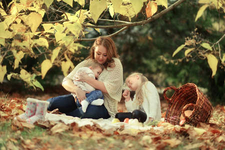 sunny autumn forest resting sitting in foliage mother with her cute childrenの写真素材