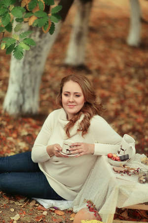 golden autumn in the forest beautiful woman with long hair with a cup in his hands on a picnicの写真素材